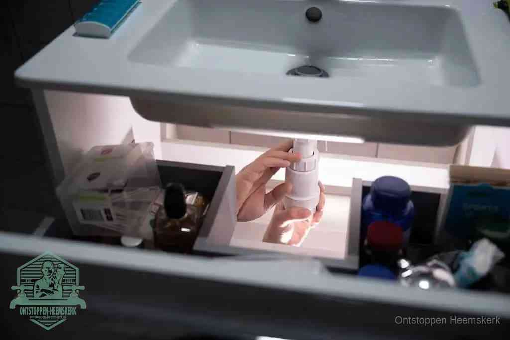 Een pompfles met zeep boven een wastafel, de heet water en afwasmiddel-methode om een vetprop in de afvoer los te maken in Heemskerk