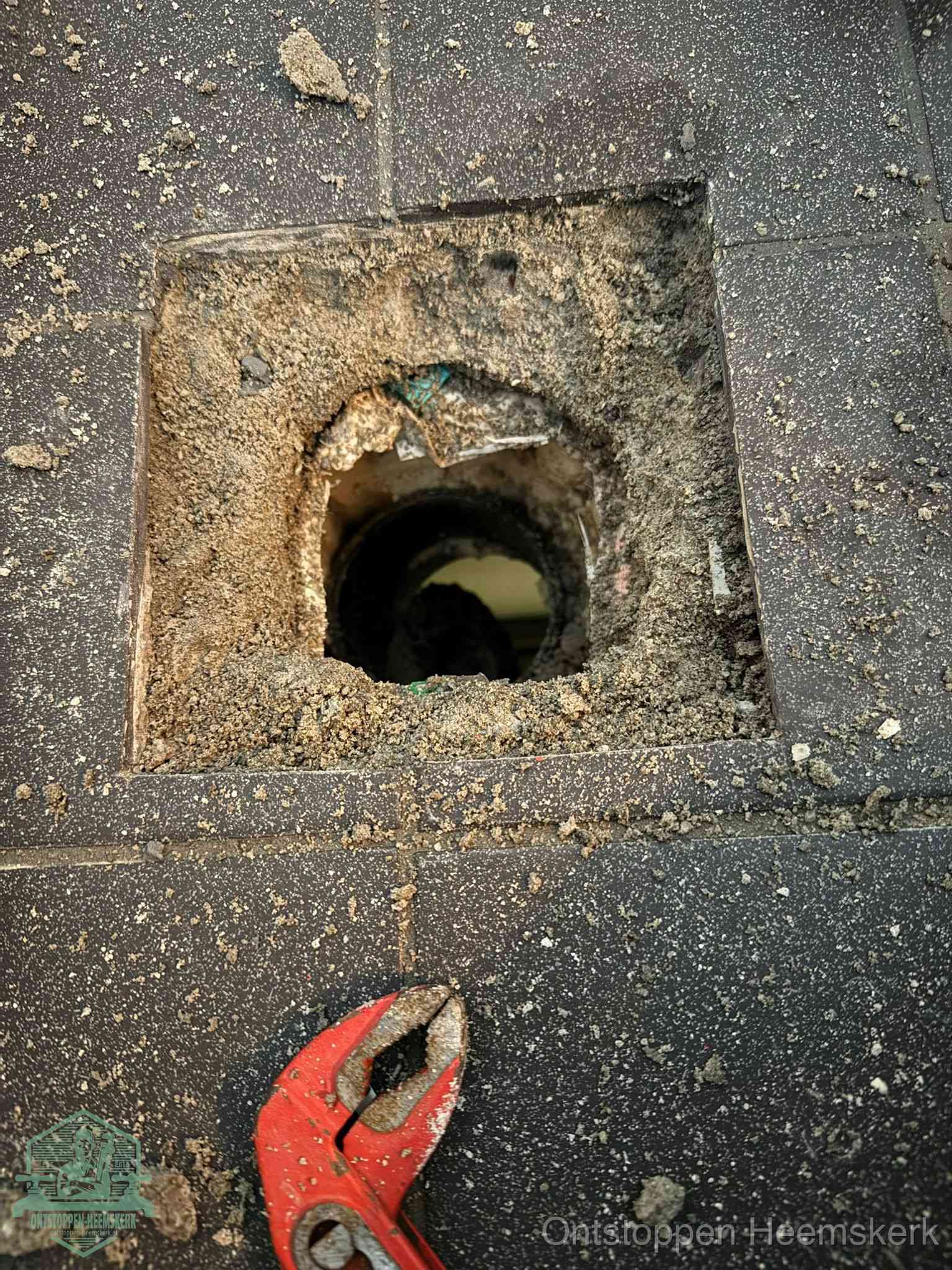 Een geopend rioolputje in een betontegelvloer met losgemaakt rooster en een zichtbare ronde afvoerbuis, het achterhalen waar de afvoerverstopping zit in Heemskerk