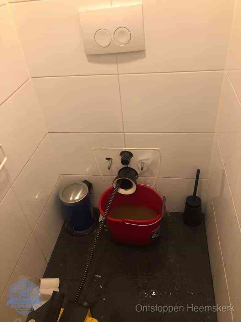 Een ontstopte wand-wc met verwijderde toiletpot waar een ontstoppingsveer in de wanduitgang verdwijnt, het achterhalen waar de verstopping zit in Heemskerk