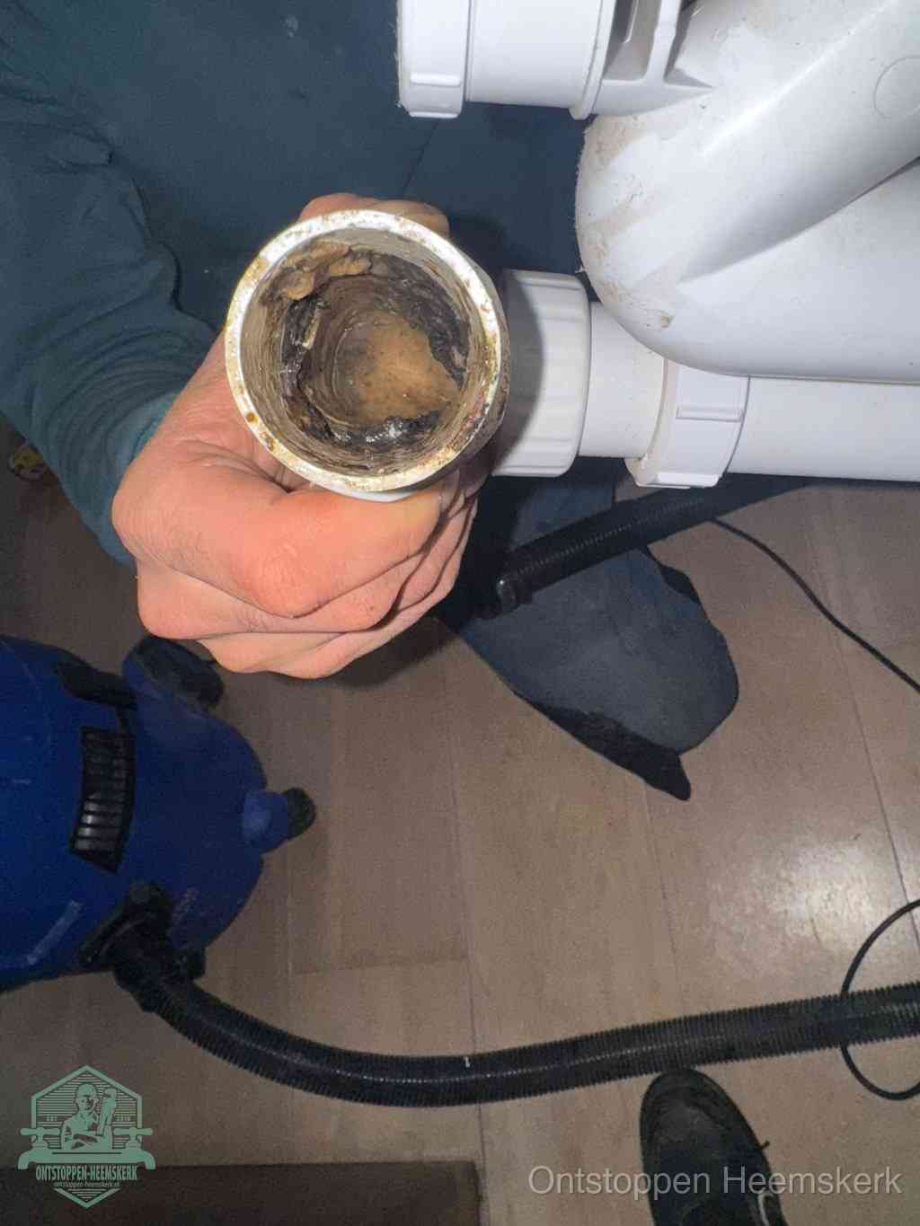 Een hand houdt een losgekoppeld PVC-afvoerbuisstuk vast dat van binnen volledig is dichtgeslibd met vet, vuil en aanslag, de meest voorkomende oorzaak van een verstopte afvoer in Heemskerk