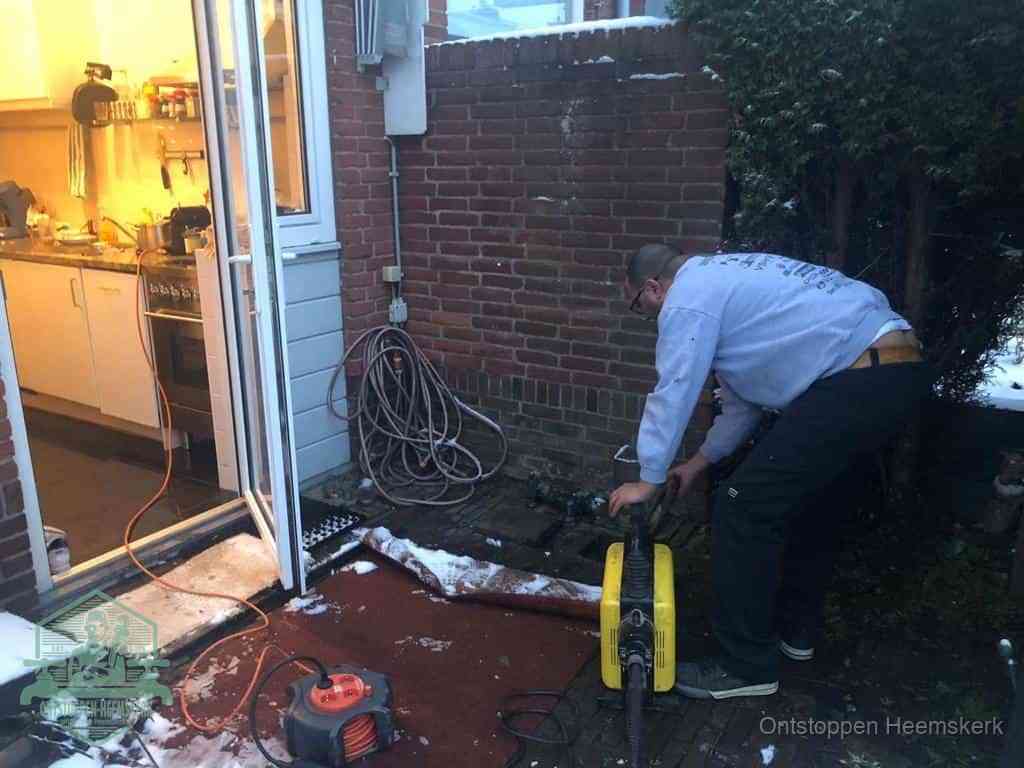 Een monteur werkt buiten bij een open riool-/grondput met een elektrische ontstoppingsmachine om een verborgen afvoerprobleem op te sporen in Heemskerk