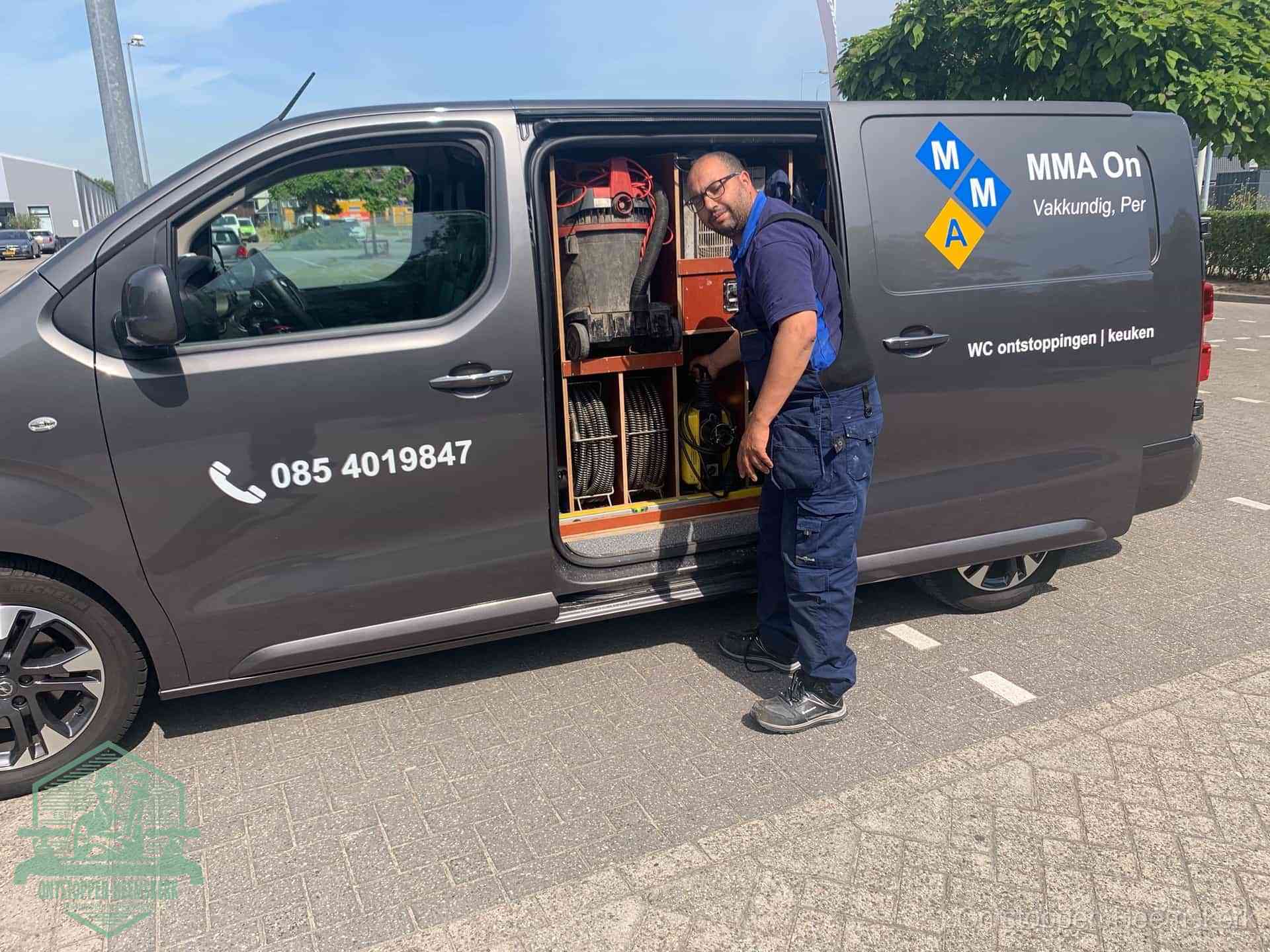 Een monteur bij de open schuifdeur van zijn bedrijfsbus op een parkeerplaats, klaar om de oorzaak van terugkerende afvoerverstoppingen aan te pakken in Heemskerk