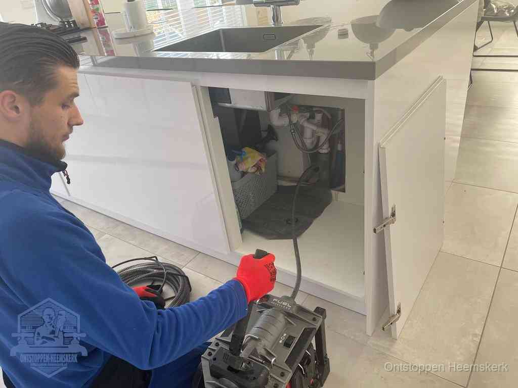 Monteur ontstopt met een veermachine een verstopte afvoer onder de gootsteen in Heemskerk
