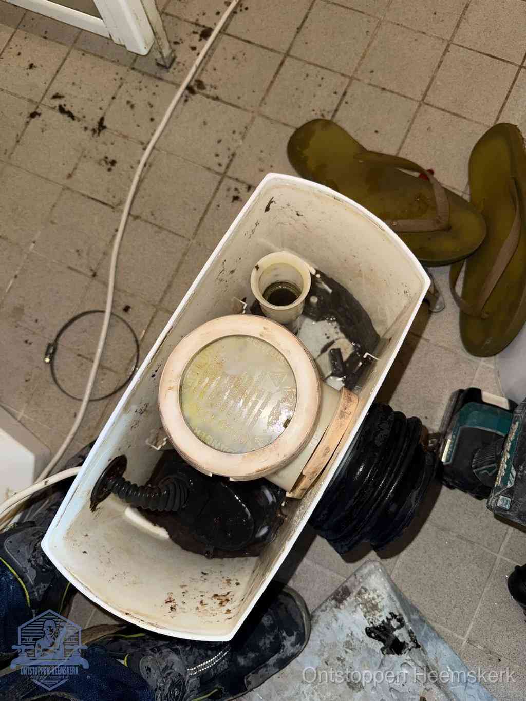 Een gedemonteerde toiletpot op de vloer met ontstoppingsveer en gereedschap ernaast, het verwijderen van een vastzittend voorwerp uit de wc in Heemskerk