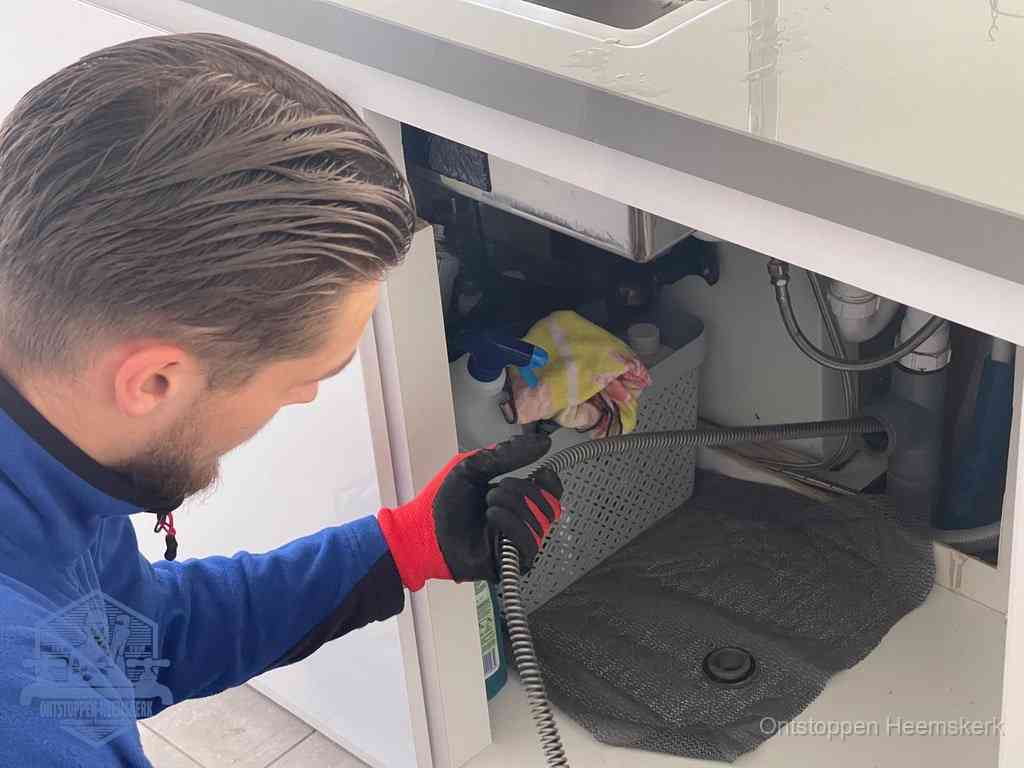 Een monteur voert een flexibele ontstoppingsveer in de afvoer om een verstopping voorbij de bocht van het toilet te bereiken in Heemskerk