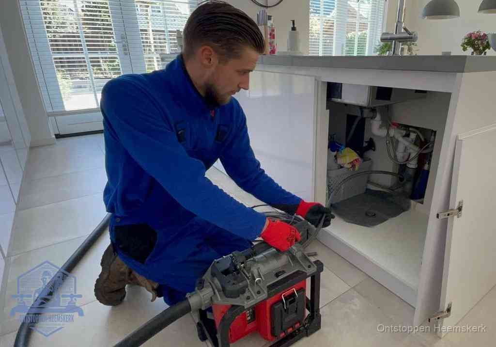 Een monteur voert een professionele elektrische ontstoppingsmachine in de afvoer onder de spoelbak tijdens het gootsteen ontstoppen in Heemskerk